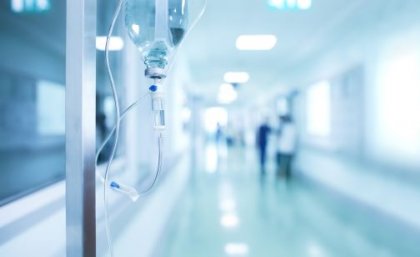 A photo showing an antibiotic drip on a stand in the foreground, with the corridor of a hospital in the blurred background. 